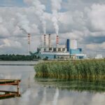 Power plant emitting smoke with a waterfront view of a lake and reeds.