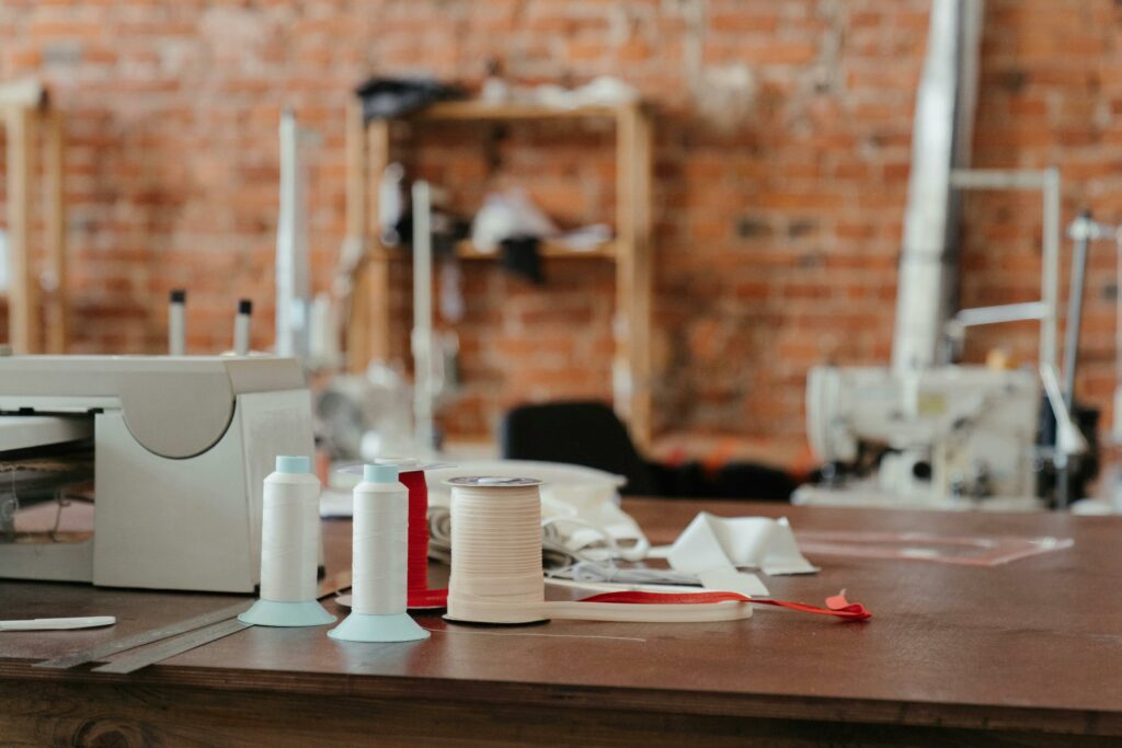 A sewing table featuring spools of thread and a sewing machine in a cozy workspace. Le côté obscur de la fast fashion.